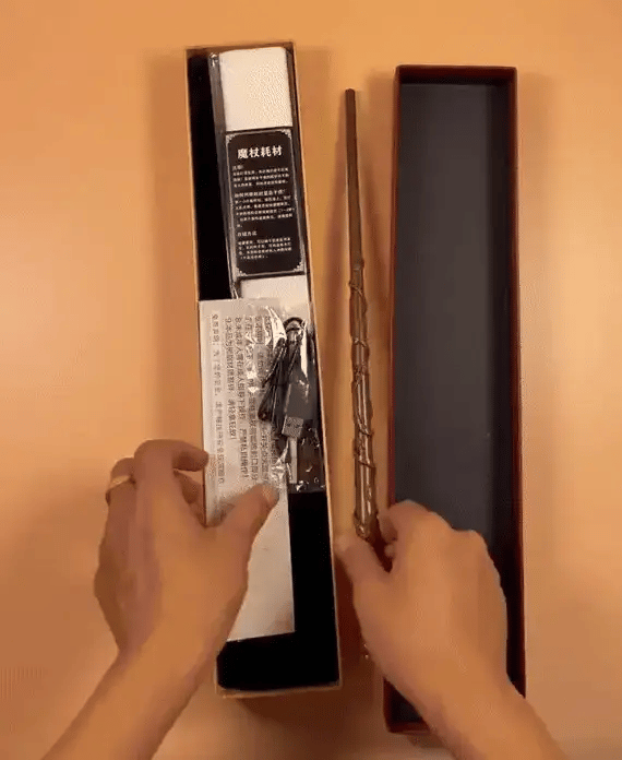 Person holding a gold wand and its packaging with a plain background